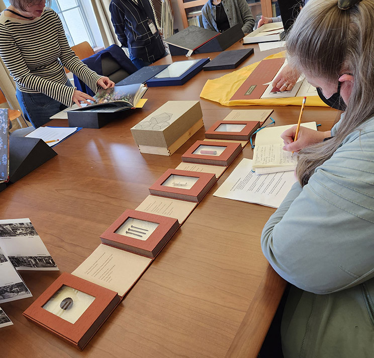 Seminar students looking at and taking notes on books at a large table