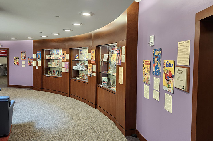 Exhibit area on 4th floor with wall-mounted comic book covers and glass cases full of items from the collection