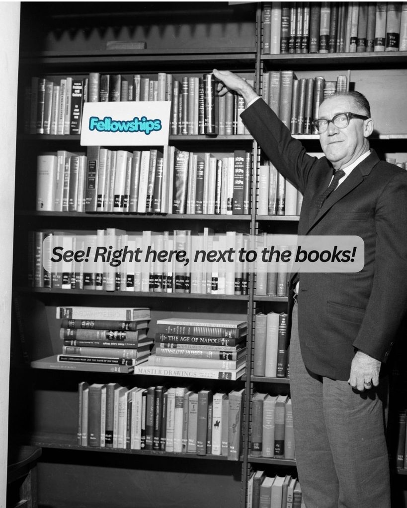 Black-and-white photograph of former Appalachian State Librarian W.L. Eury reaching up to touch a book on a tall library shelf. A small white card resting on an upper shelf reads "Fellowships" in blue font, and overlay text across the middle of the image reads, "See! Right here, next to the books!".
